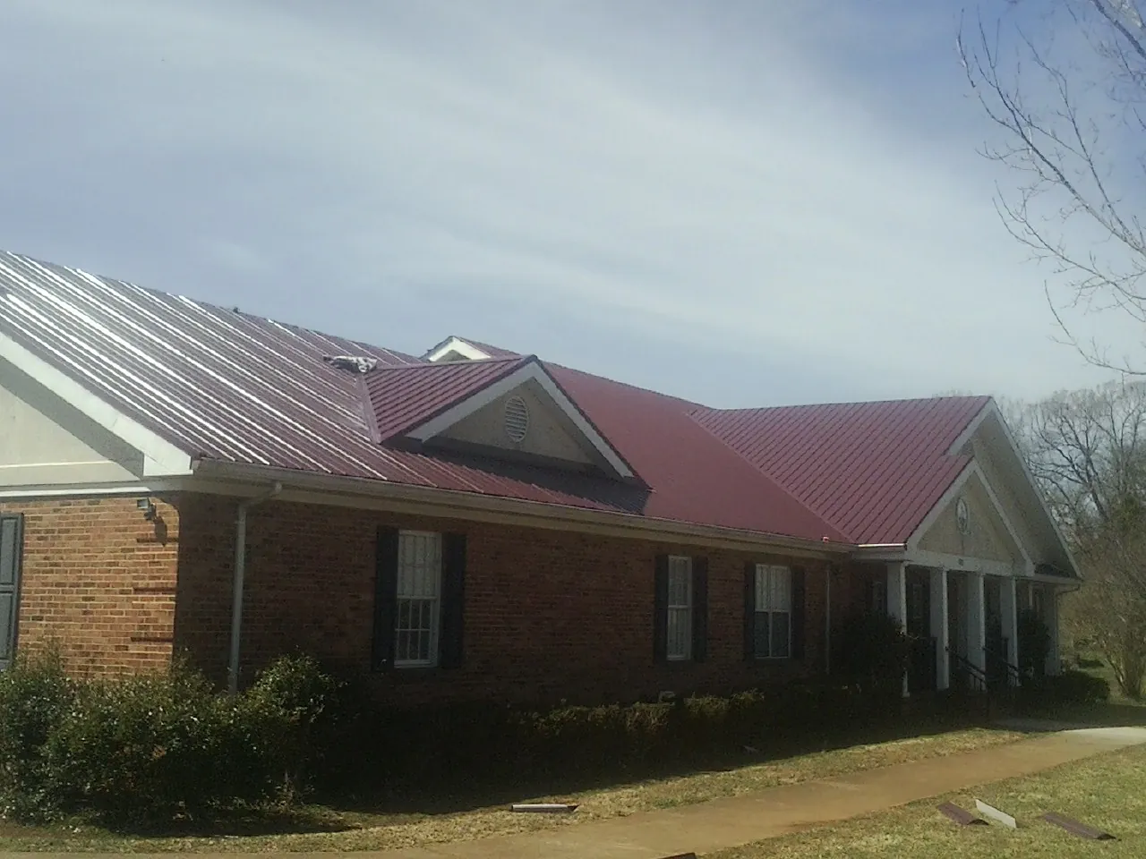 Red metal roof with gabled entries on a long brick building, from a Hail Damage Roof Repair job in Moxee