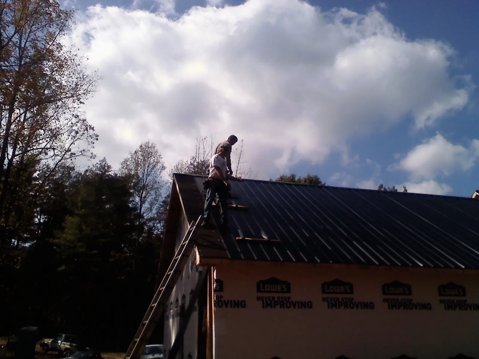 Roofer fastening dark metal panels high against a cloudy sky, from a Roof Inspection job in Moxee