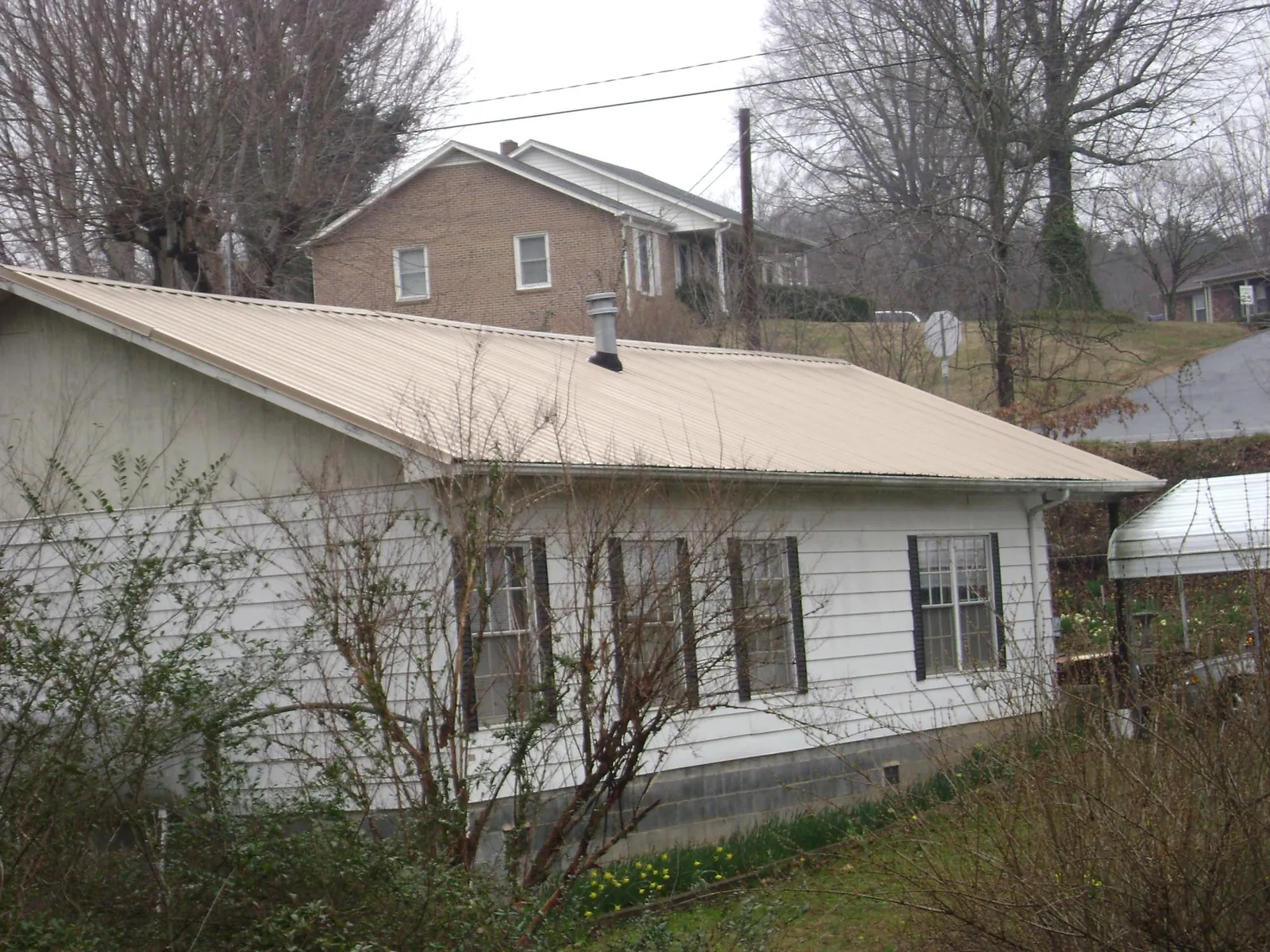 Tan metal roof on a white sided house set into a hillside — Commercial Roofing by Roofing Brothers in Moxee